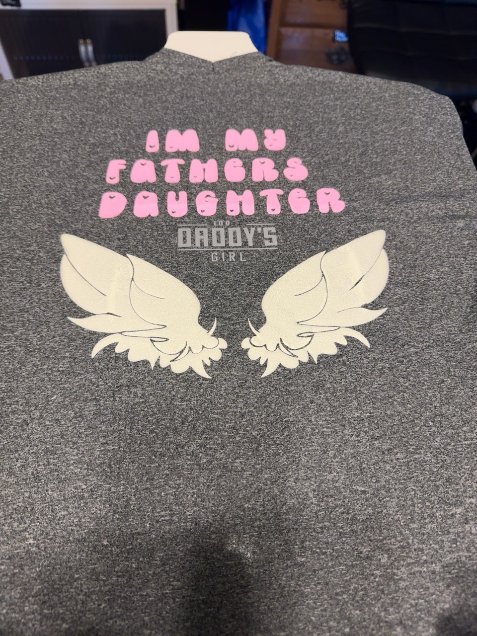 Finished heather-gray father’s daughter shirt with pink lettering and cream angel wings, made by Chevelle’s Customs.